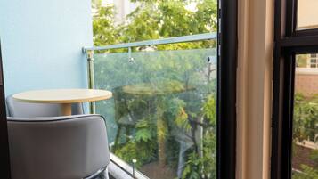 Un balcón con una mesa, una silla y barandilla de vidrio, y vistas a la vegetación.