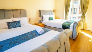 Quarto de hotel com duas camas, piso de madeira e janela com cortinas.