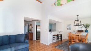 Una sala de estar moderna con un sofá azul, una mesa de comedor de madera con sillas y una cocina al fondo.