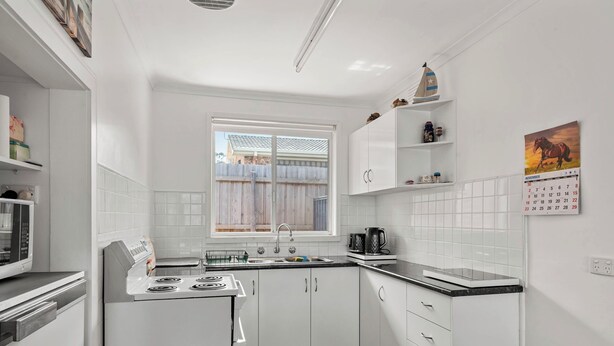A modern kitchen with white cabinets, a stove, and a window with a view of a wooden fence. - Central Unit in Chapel, Cowes (Cowes)