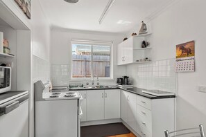 Eine moderne Küche mit weißen Schränken, einem Herd und einem Fenster mit Blick auf einen Holenzaun.