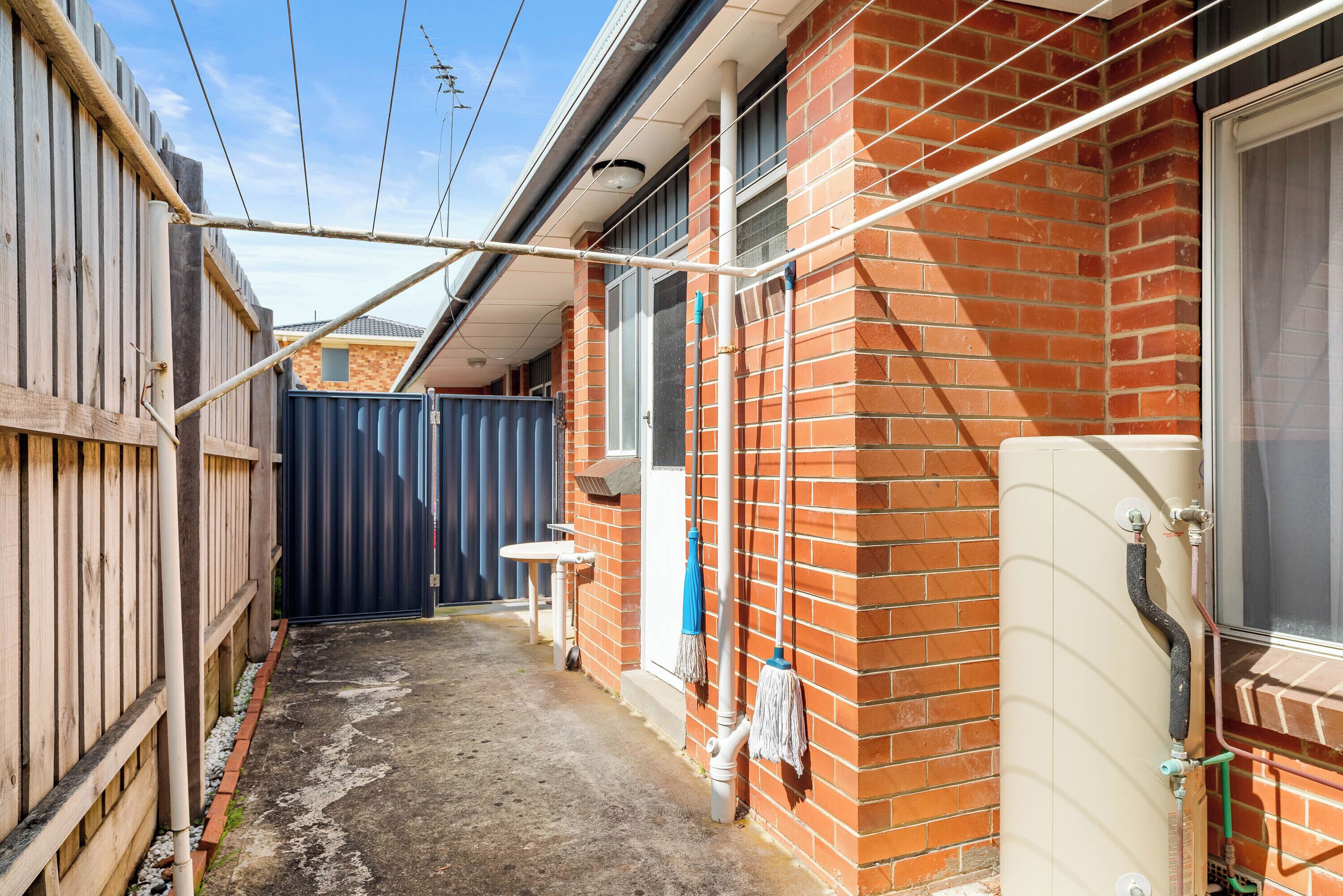 A narrow alleyway with a brick building, a wooden fence, and a blue gate.