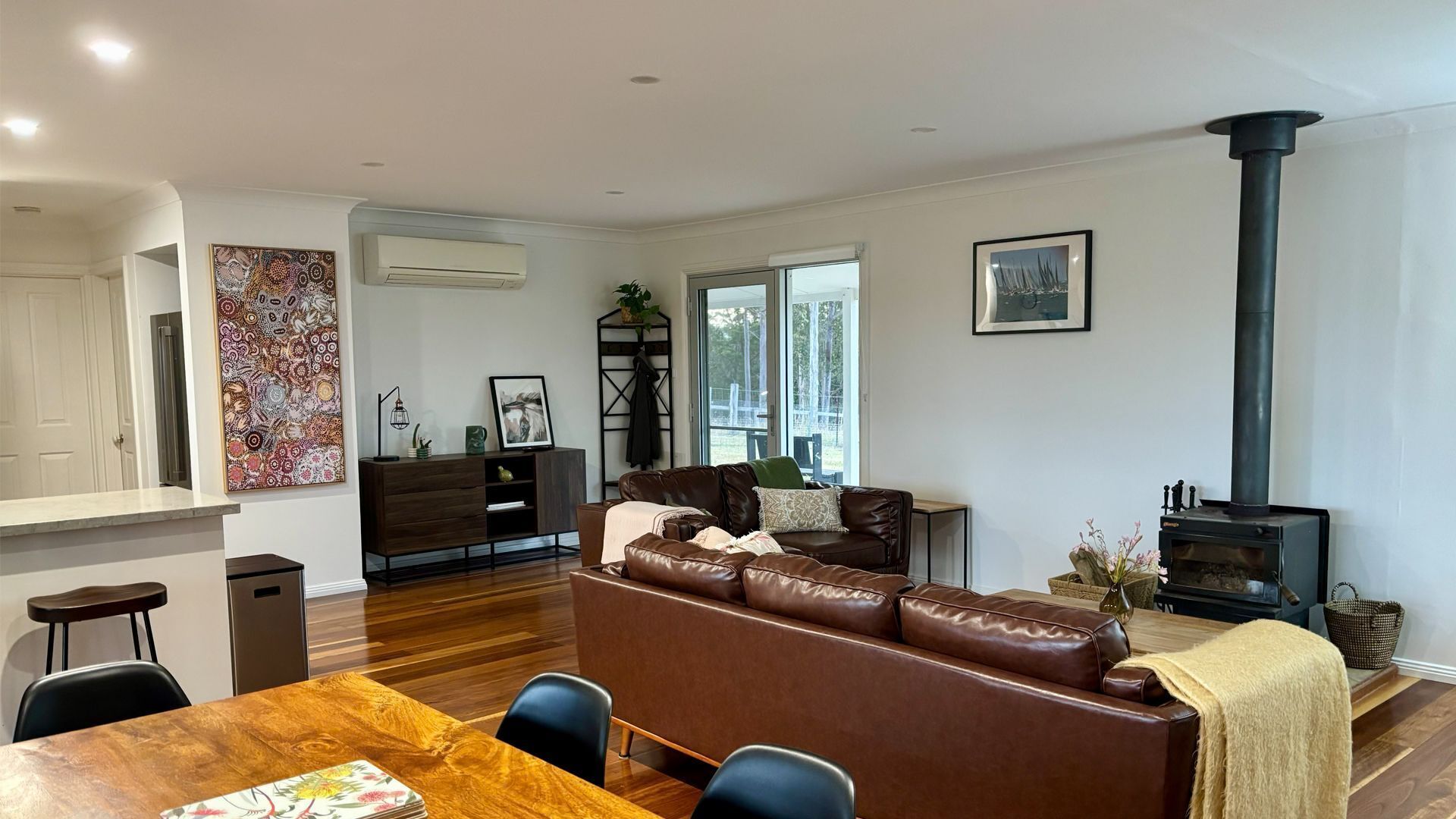 A modern living room with a brown leather sofa, a dining table with chairs, a fireplace, and a large window.