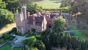 Un edificio grande e histórico con una torre destacada, rodeado de jardines cuidados y un amplio césped.