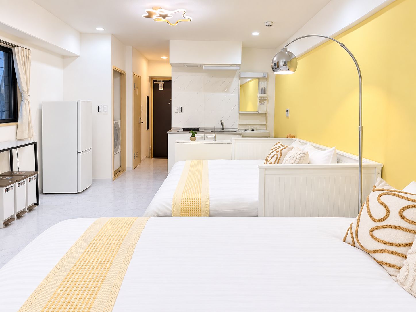 A modern hotel room with a bed, bedside table, and a kitchenette.