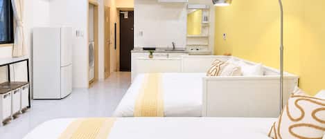 A modern hotel room with a bed, bedside table, and a kitchenette.
