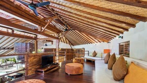 Un vaste espace de vie doté d’un plafond haut, de poutres en bois, d’un téléviseur et d’un canapé agrémenté de coussins.