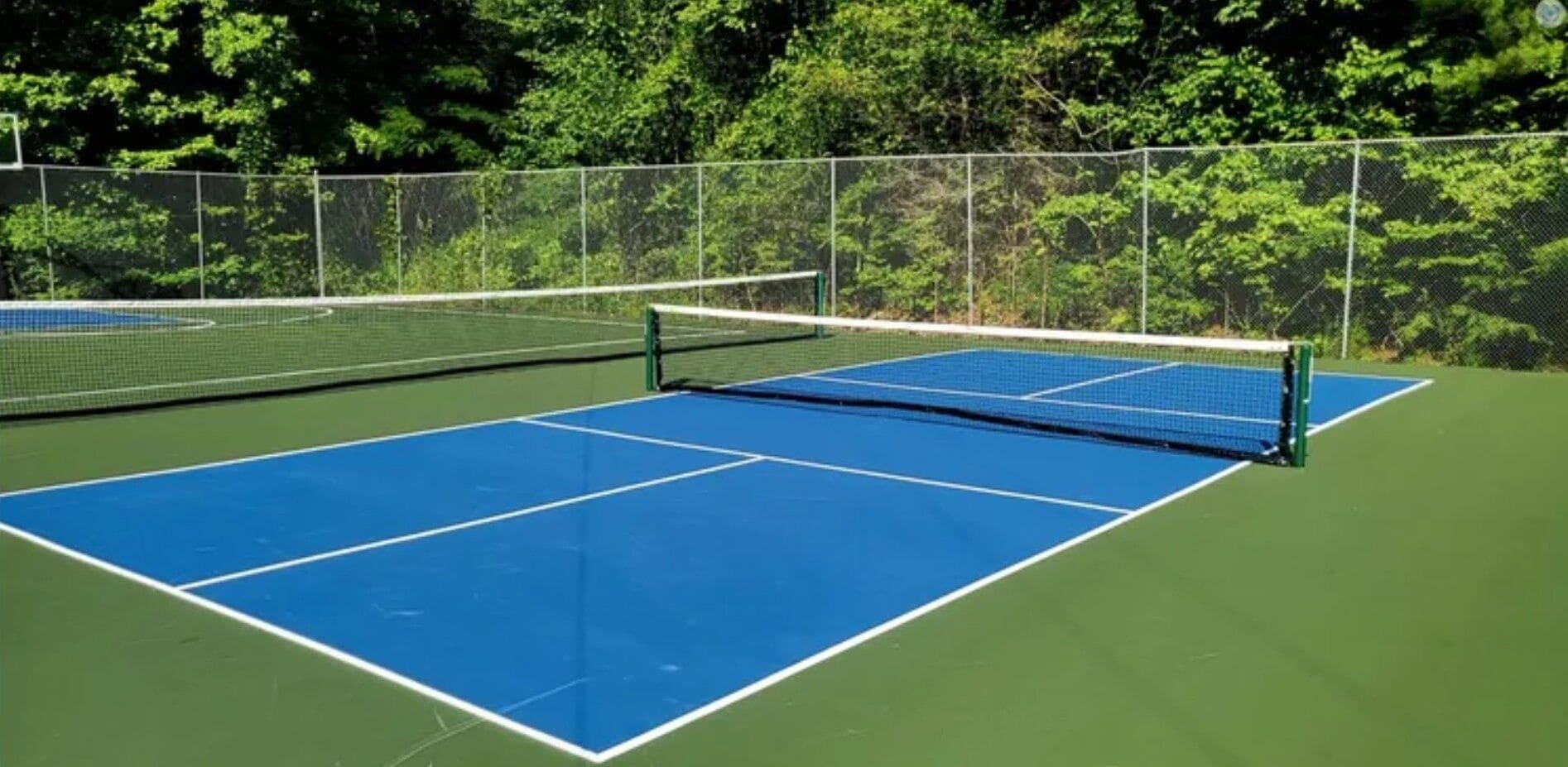 Ein Tennisplatz mit Netz in der Mitte, umgeben von einem Zaun und Bäumen.