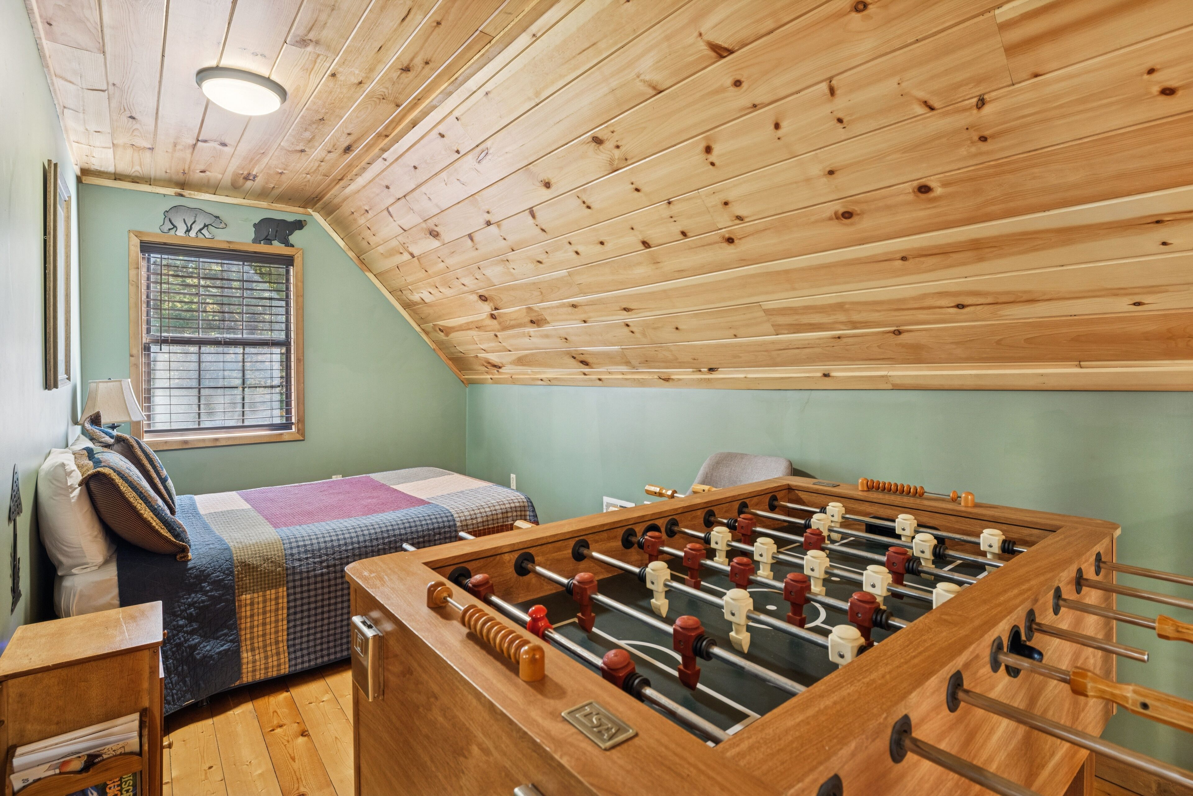 Ein gemütliches Zimmer mit Holzbalkendecke, einem Bett mit kariertem Überwurf und einem Kicker.