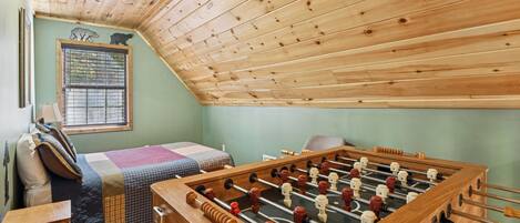 Ein gemütliches Zimmer mit Holzbalkendecke, einem Bett mit kariertem Überwurf und einem Kicker.