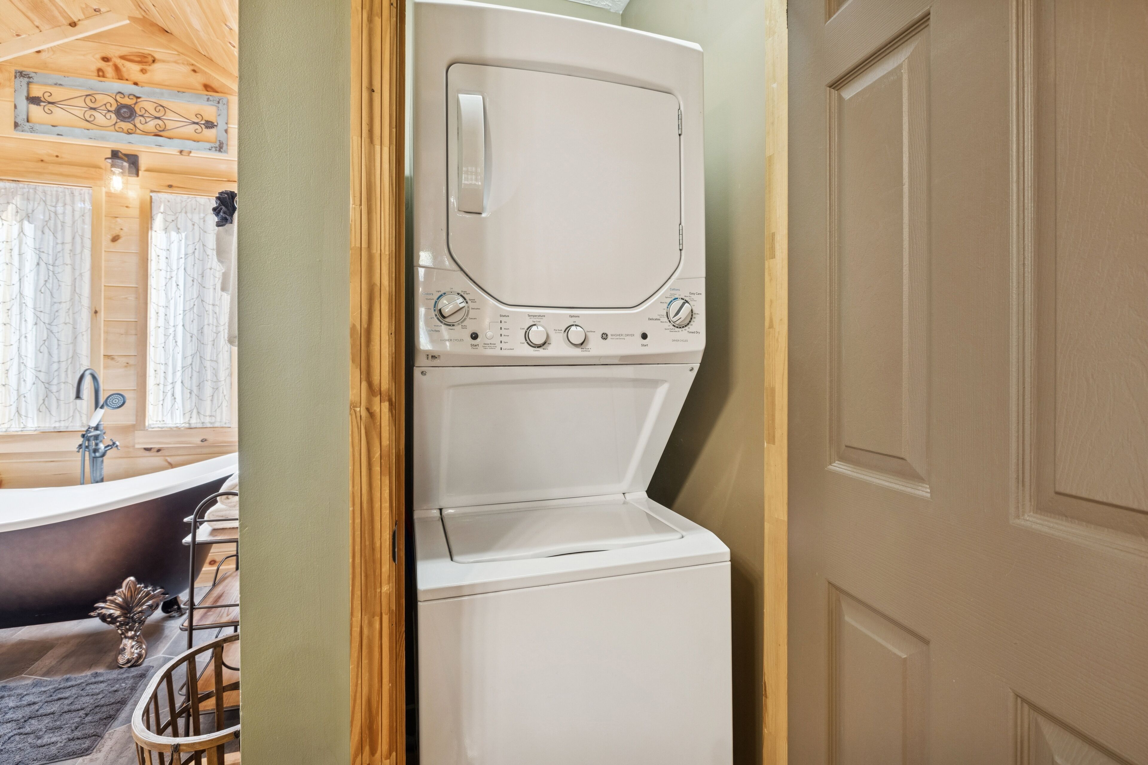 A compact laundry room with a front-loading washer and dryer, a bathtub, and a wooden interior.