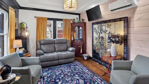 Ein Wohnzimmer mit Ledersofa, zwei Sesseln, einem gemusterten Teppich, einer Holzkommode und einem traditionellen Wandbild.