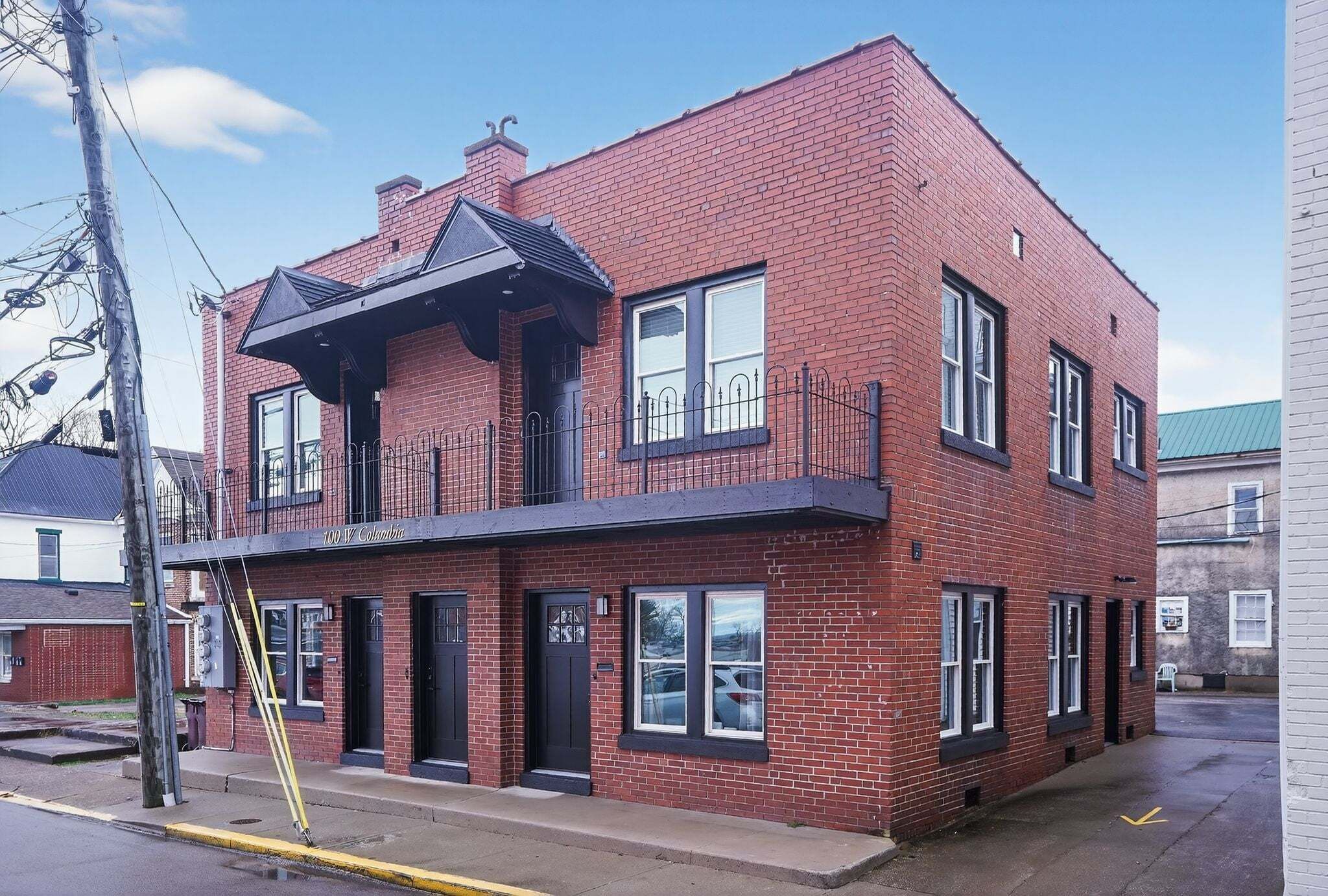 A two-story brick building with a black awning over the entrance, a visible garage door, and a small balcony with a black railing.