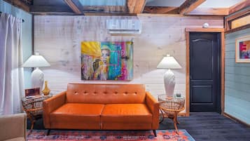 A room with a leather sofa, two side tables with lamps, a colorful abstract painting, and a patterned rug.