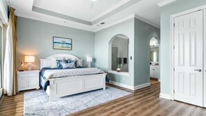 Una camera da letto con un letto, comodini, una ventola a soffitto, una finestra con tende e una porta.