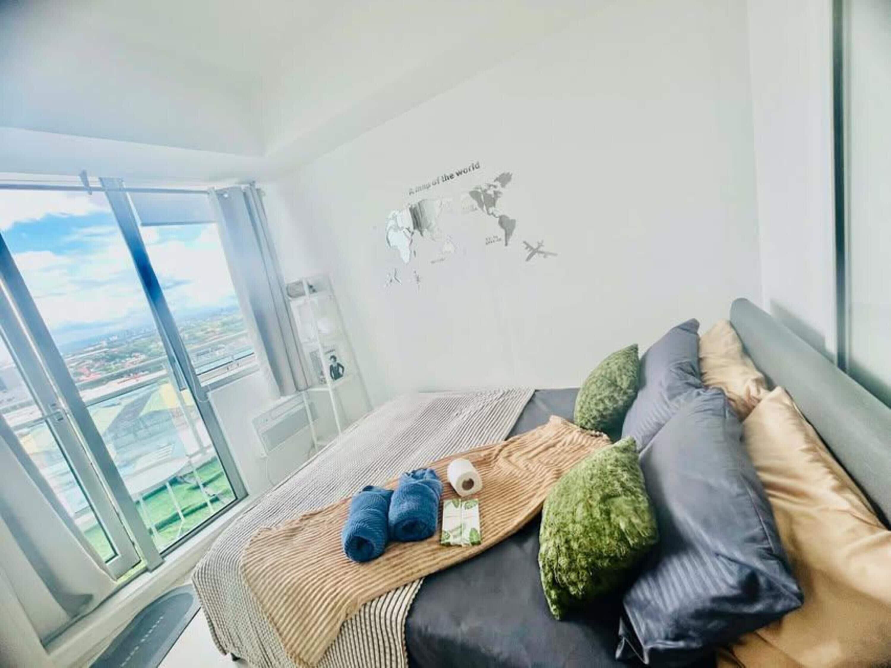 A hotel room with a large window, a bed with pillows, a blanket, and a wall decoration.