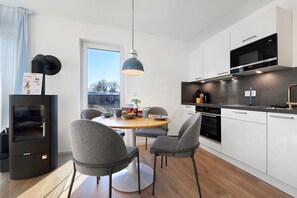 Una cocina moderna con horno empotrado, microondas y una zona de comedor con una mesa redonda y sillas grises.