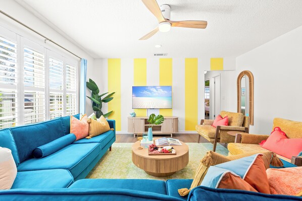 Ein modernes Wohnzimmer mit einem blauen Sofa, einem runden Couchtisch und einer Wand im Streifenmuster aus Gelb und Weiß.