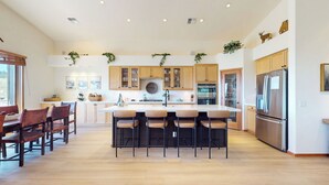 Una cocina amplia con armarios de madera, una isla central con taburetes de bar, un refrigerador de acero inoxidable y un ventanal que proporciona luz natural.