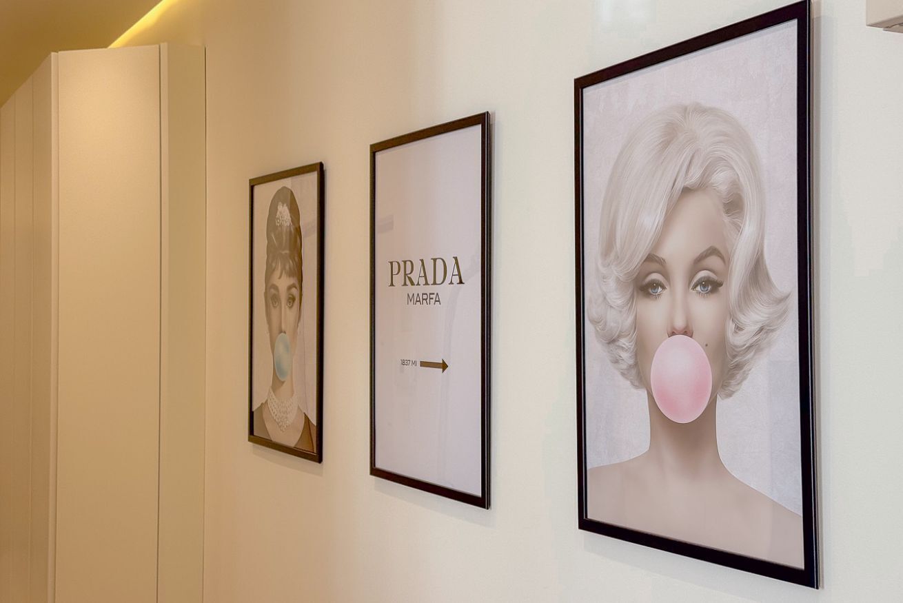 Trois tableaux encadrés sont accrochés au mur : l’un porte l’inscription « PRADA MARFA 1837 » et l’autre représente une bulle de chewing-gum rose.
