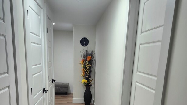 A hallway with white doors, a wooden floor, and a wall-mounted clock. - Beautiful Oasis Haven 1 Bedroom unit (Moncton)