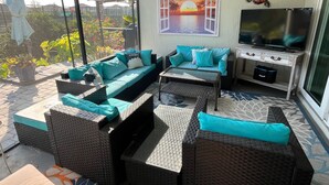 Salón soleado con sofá, mesa de centro y televisor, con vistas a un jardín.