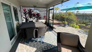 Un patio soleado con mesa y sillas, un ventilador de techo y vistas a un jardín ajardinado.