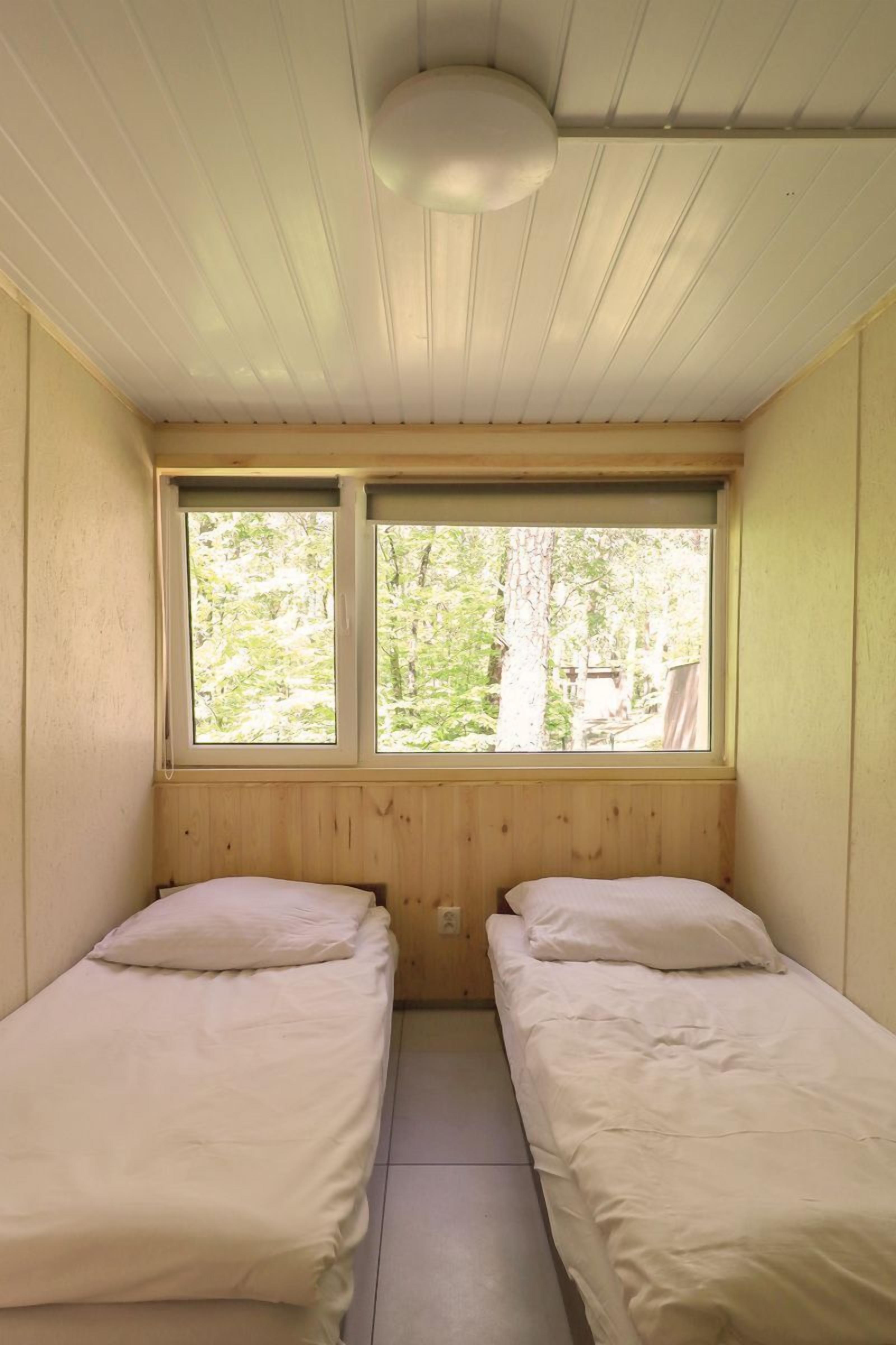 Una habitación pequeña con dos camas individuales, paredes de madera, techo inclinado y ventana con vistas a la vegetación.