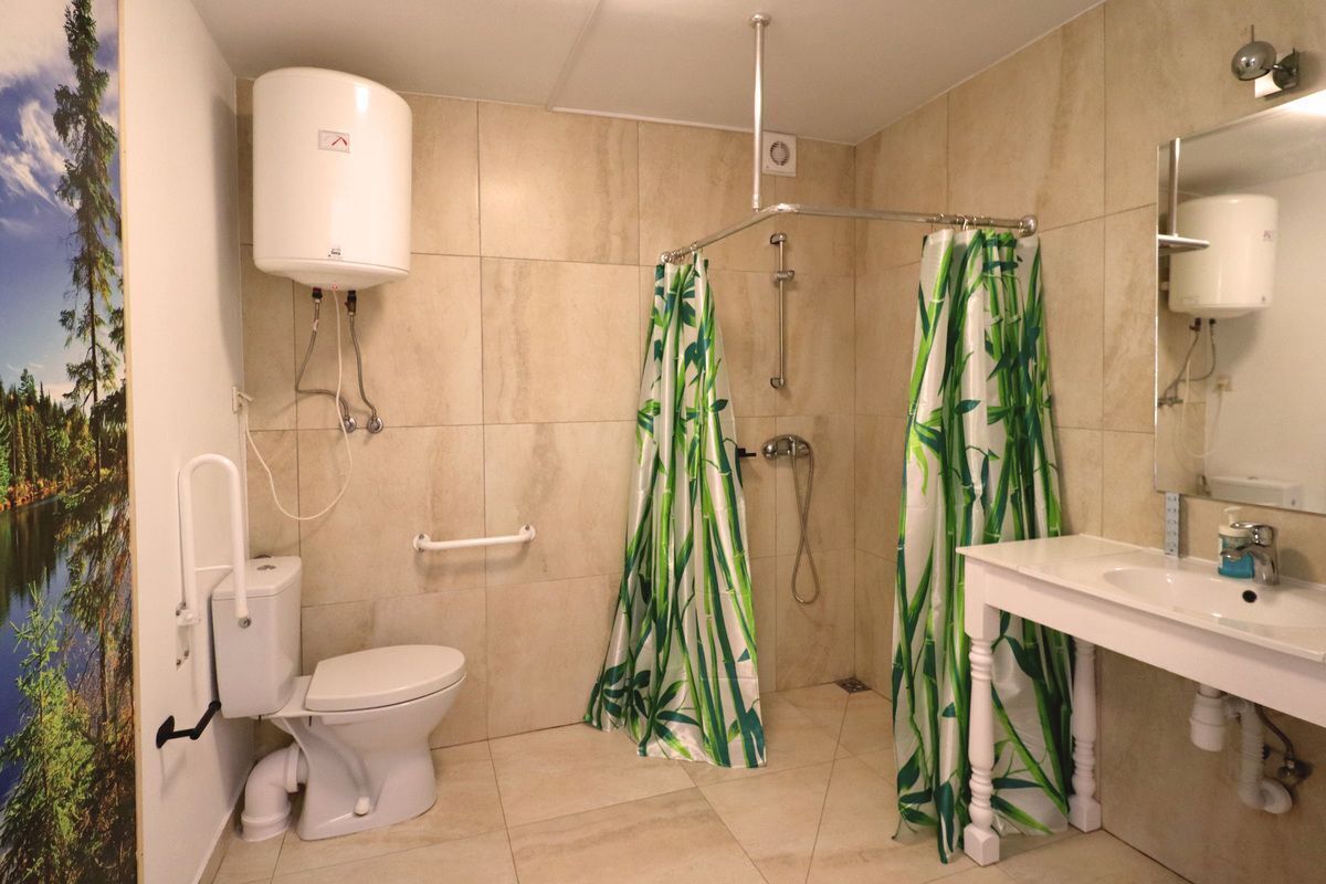 Un baño con inodoro, lavamanos, ducha con cortina de bambú y calentador de agua montado en la pared.