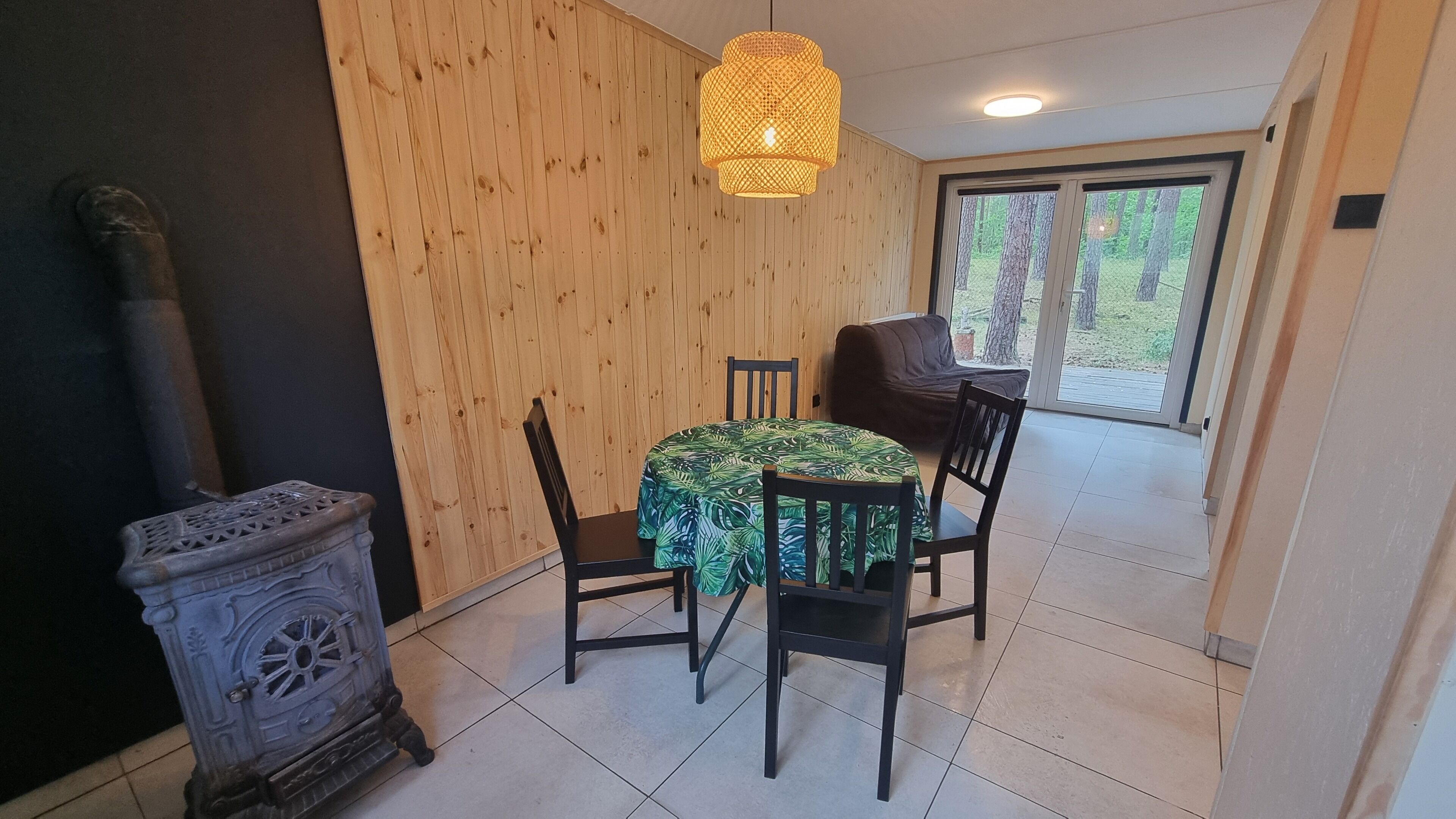 A dining area with a table set for four, a wooden wall, a large window, and a hanging light fixture.