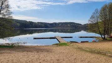 Un lago tranquilo con un muelle de madera que se adentra en el agua, rodeado de árboles y una playa de arena.