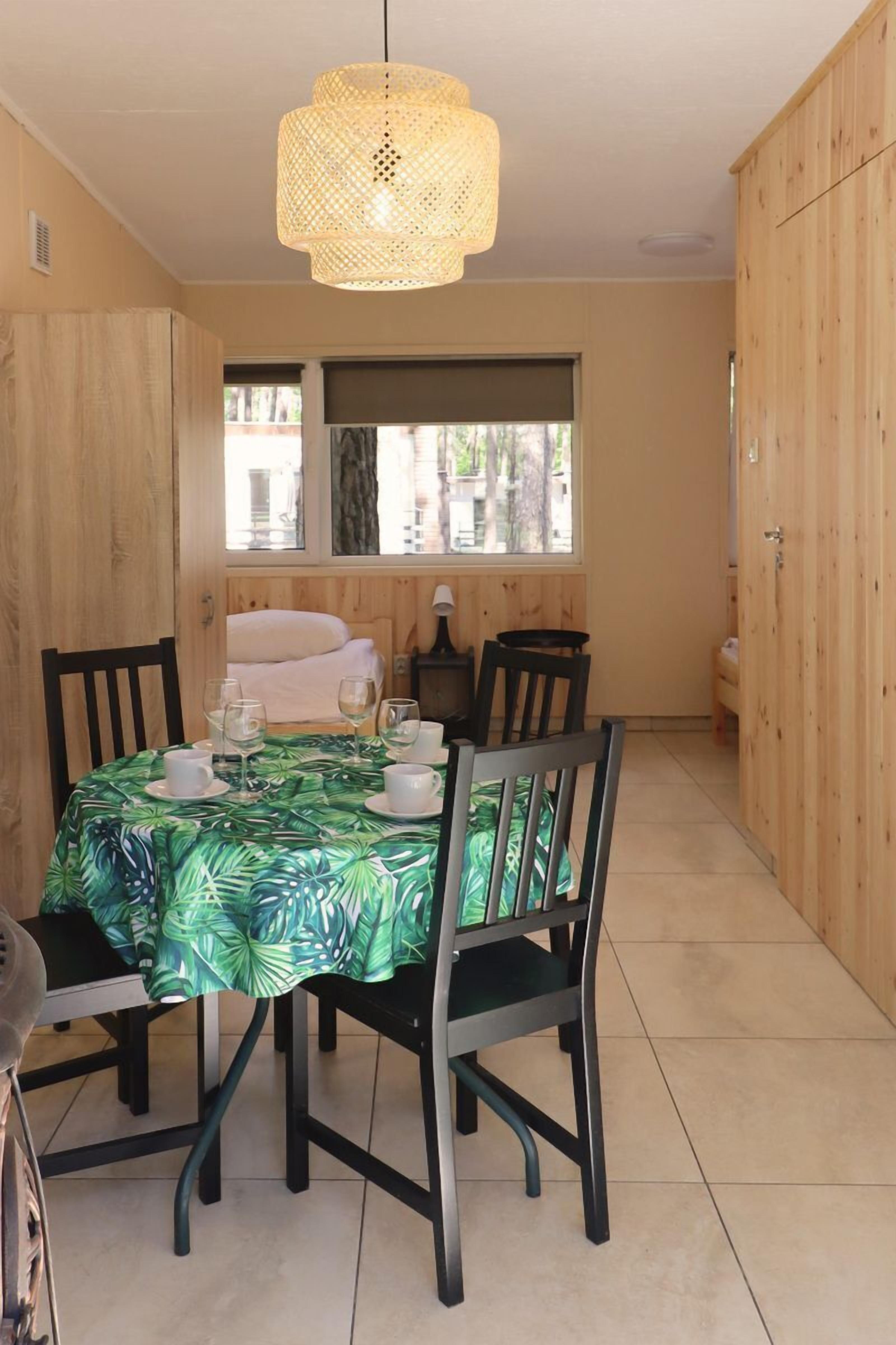 Un coin repas avec une table dressée pour quatre personnes, des chaises, un luminaire suspendu et une vue par la fenêtre.