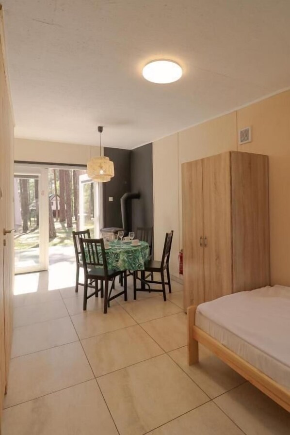 Une pièce comprenant un lit, une armoire en bois, une table à manger avec des chaises, et donnant sur un jardin grâce à une porte vitrée.