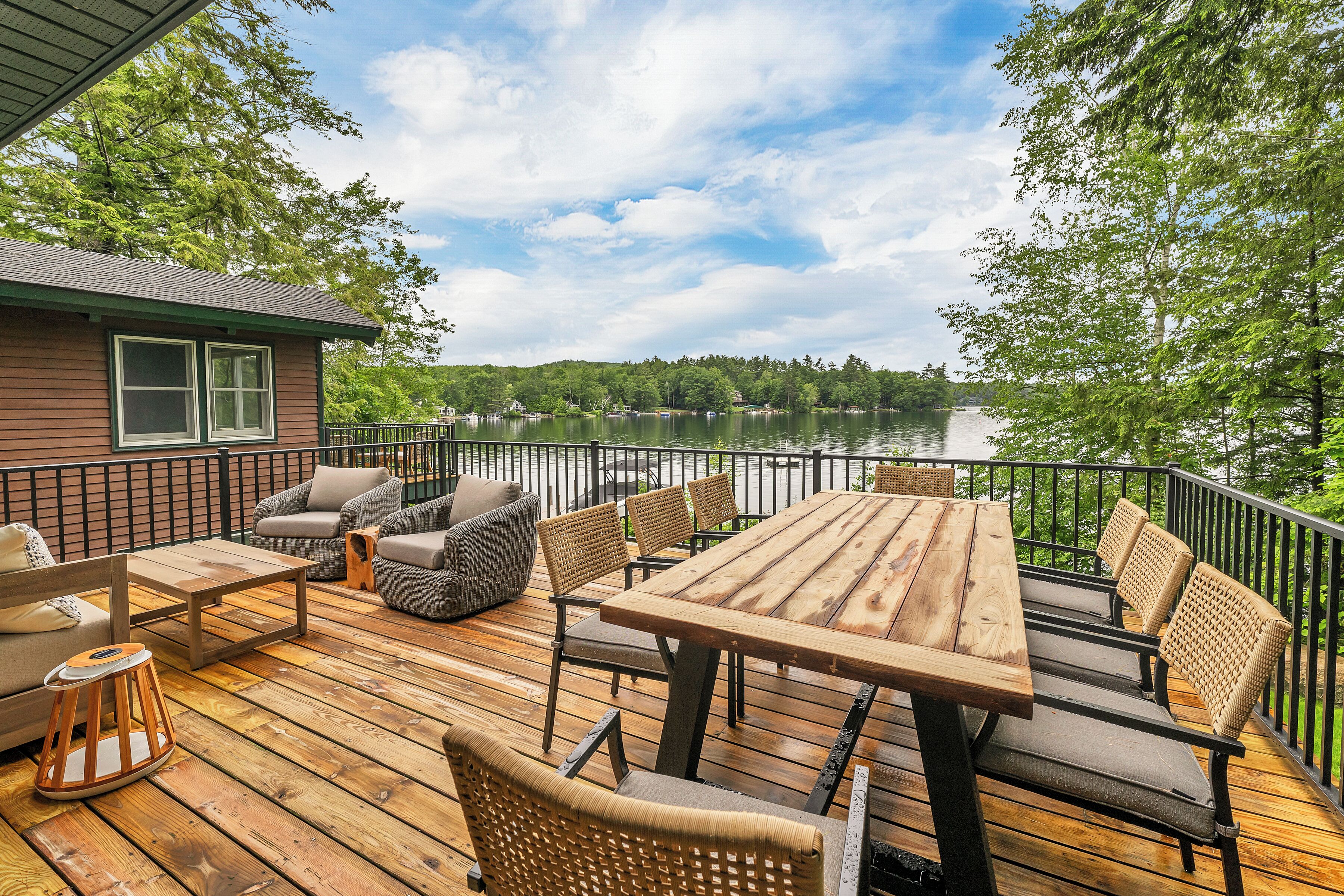 Une terrasse en bois, aménagée avec du mobilier d’extérieur, notamment une table et des chaises, donnant sur un lac.