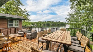 Une terrasse en bois, aménagée avec du mobilier d’extérieur, notamment une table et des chaises, donnant sur un lac.