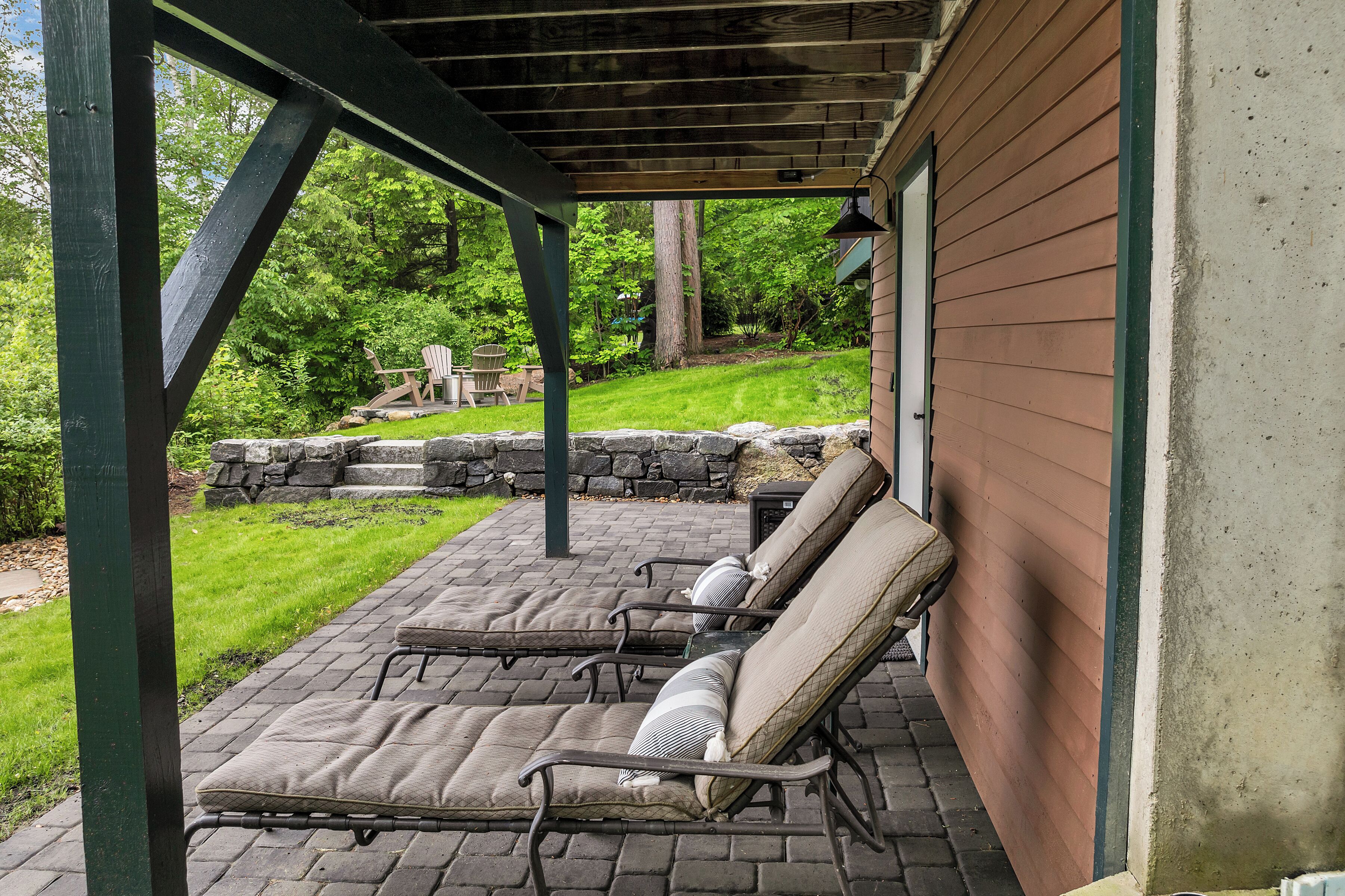 A covered patio with four lounge chairs and a stone wall.