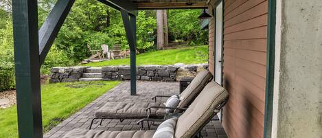 A covered patio with four lounge chairs and a stone wall.