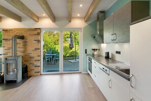 A modern kitchen with a built-in stove, white cabinetry, and a large sliding glass door leading to an outdoor patio. - Holiday Home 'Ferienhaus Hofmeyer' with Private Terrace, Private Garden and Wi-Fi (Hofgeismar)