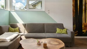 Un salon avec un canapé, une table basse et une vue sur une forêt par la fenêtre.