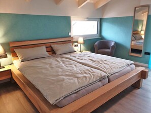 A double bed with a wooden frame, two bedside tables, a chair, a window, and a mirror on the wall. - Holiday Home 'Ferienhaus Hofmeyer' with Private Terrace, Private Garden and Wi-Fi (Hofgeismar)