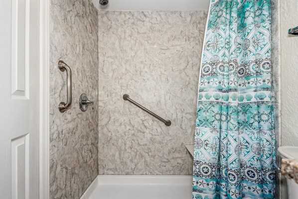 Un baño con ducha, paredes de mármol y cortina de ducha estampada.