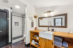 Ein Badezimmer mit einem weißen Waschbecken, einer Holzwaschmöbel-Anrichtung, einem großen Spiegel und einer Duschkabine mit einem schwarz-weißen Vorhang.
