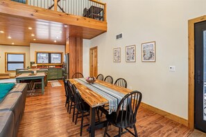 A dining area with a wooden table and chairs, a kitchen in the background, and artwork on the walls. - Brand New and Terrific Too! Welcome to Tuckered Out! (Canaan Valley)