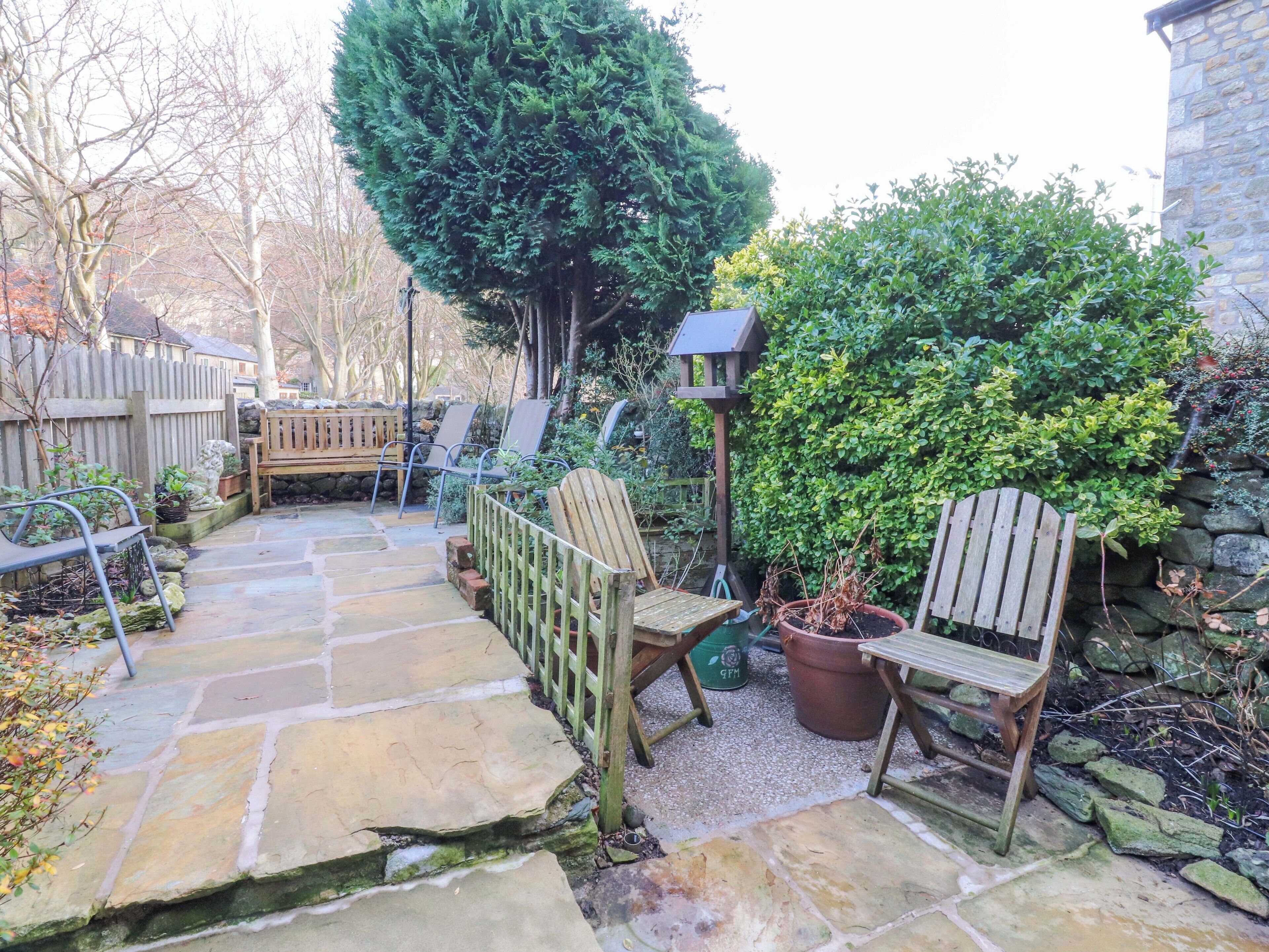 A stone patio with wooden chairs and a bird feeder.