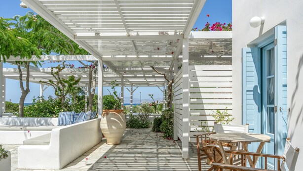 A covered outdoor seating area with a pergola, stone flooring, and a view of the sea. - Beachfront Ios Villa (Ios)