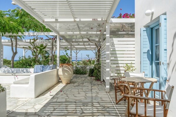 A covered outdoor seating area with a pergola, stone flooring, and a view of the sea.