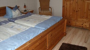 A bedroom with a wooden bed, a wicker chair, and a wooden wardrobe. - Apartment Ingrid Alfes, Apartment 1 (Lennestadt-Halberbracht)