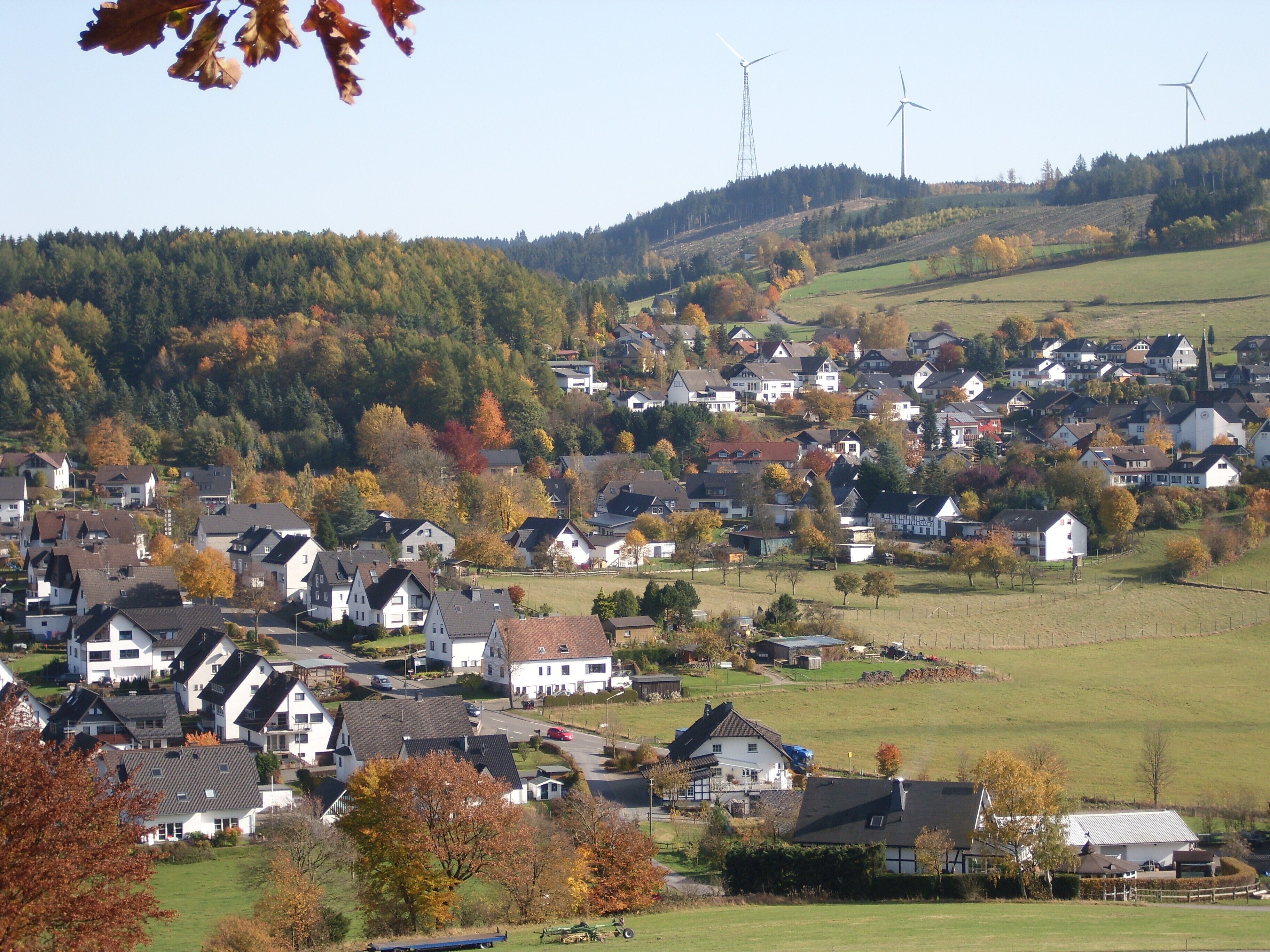 A residential area with houses, wind turbines, and autumn foliage.