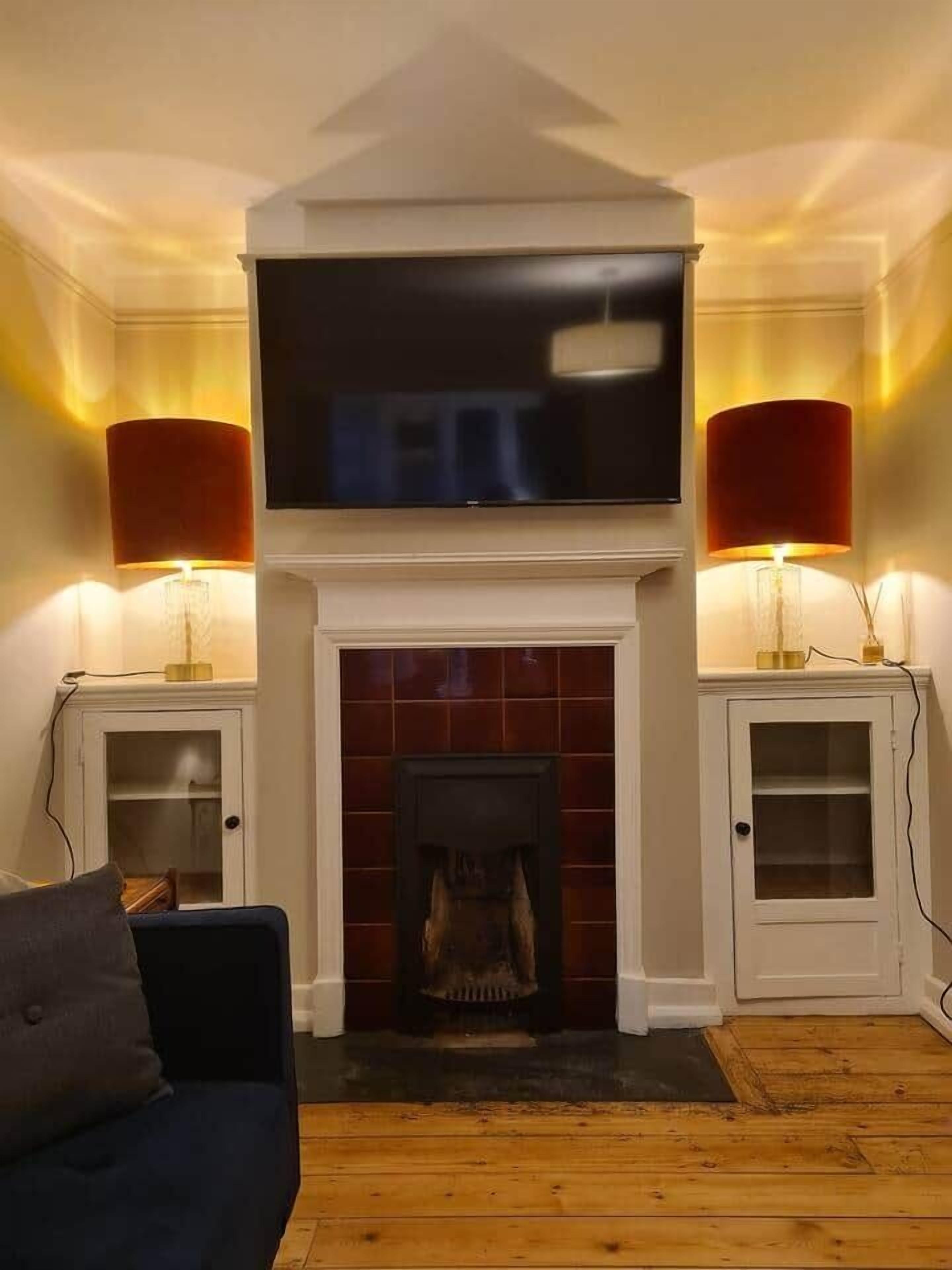 A living room with a fireplace, a television mounted above it, and two lamps on either side.
