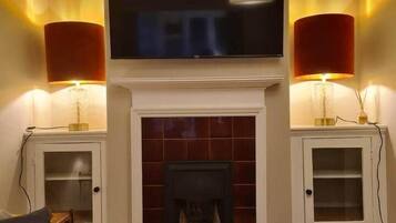 A living room with a fireplace, a television mounted above it, and two lamps on either side.